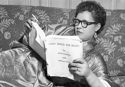 Imagen rectangular en blanco y negro de Billie Holliday, con gafas de vista, reclinada en un sofá, leyendo un libro de Blues. Imagen perteneciente a la categoría libros, de la web allanamientodemirada.com, Editorial musical y literaria.